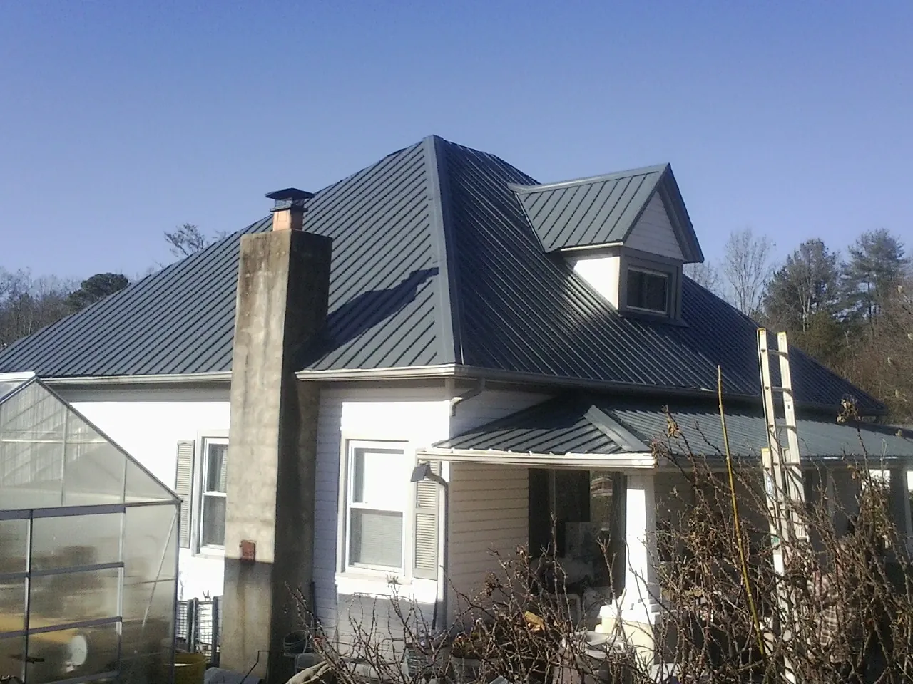 Dark blue standing seam metal roof on a white farmhouse with dormer — Slate & Tile Roof Repair by Roofing Brothers in Morrisville