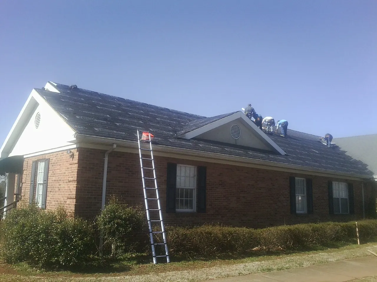 Crew tearing shingles off a brick ranch roof with a ladder set — Metal Roof Repair work by our crew in Morrisville