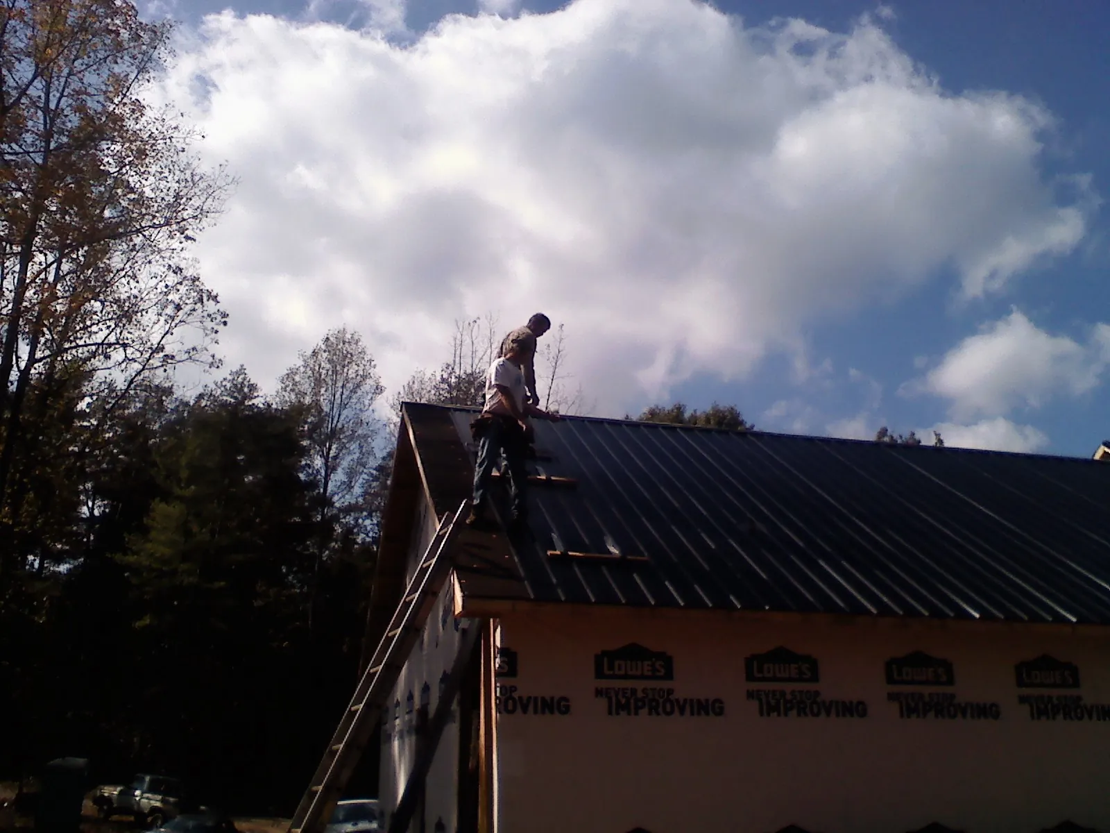 Roofer fastening dark metal panels high against a cloudy sky, from a Roof Inspection job in Morrisville