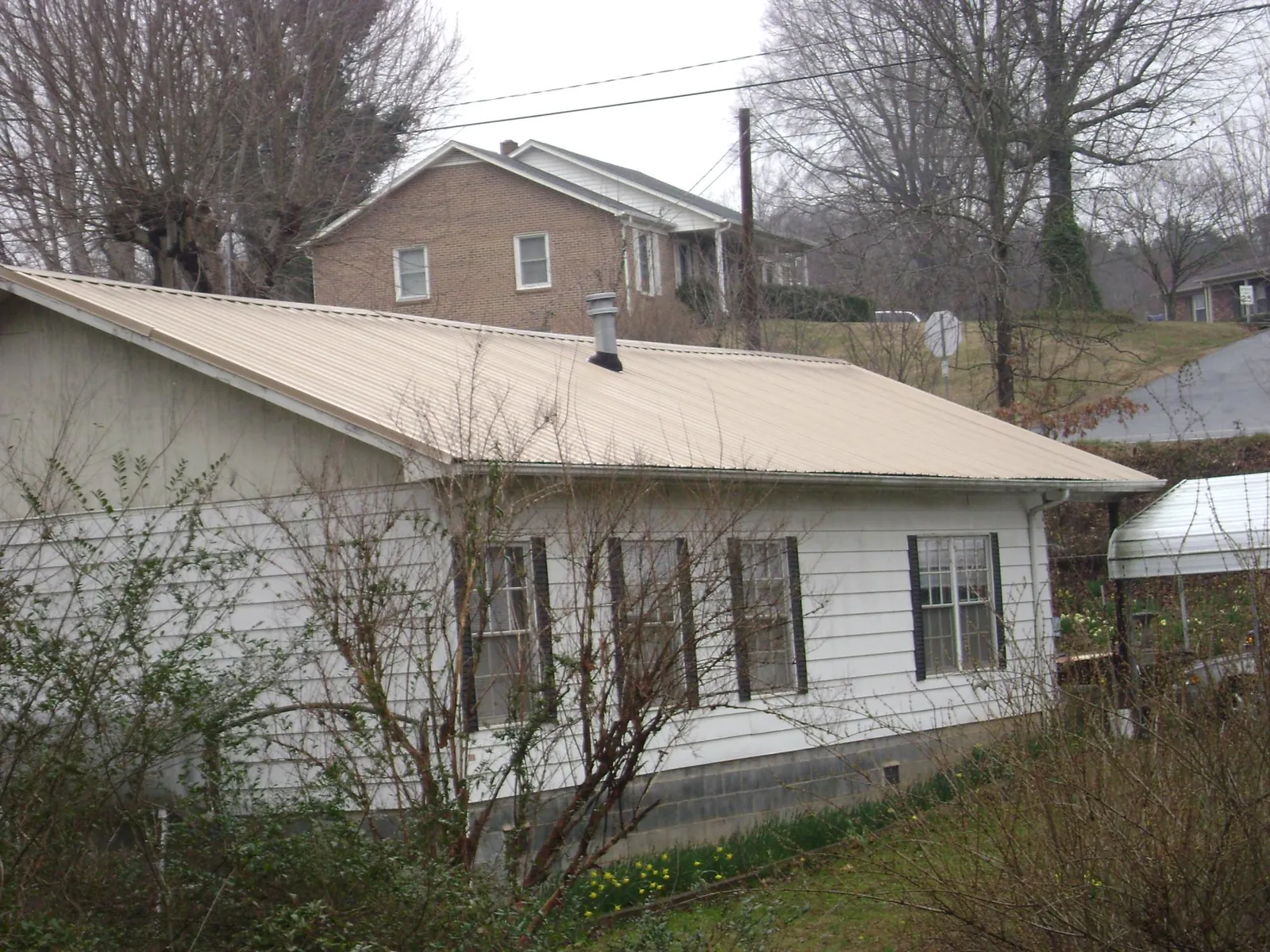 Tan metal roof on a white sided house set into a hillside — Commercial Roofing by Roofing Brothers in Morrisville