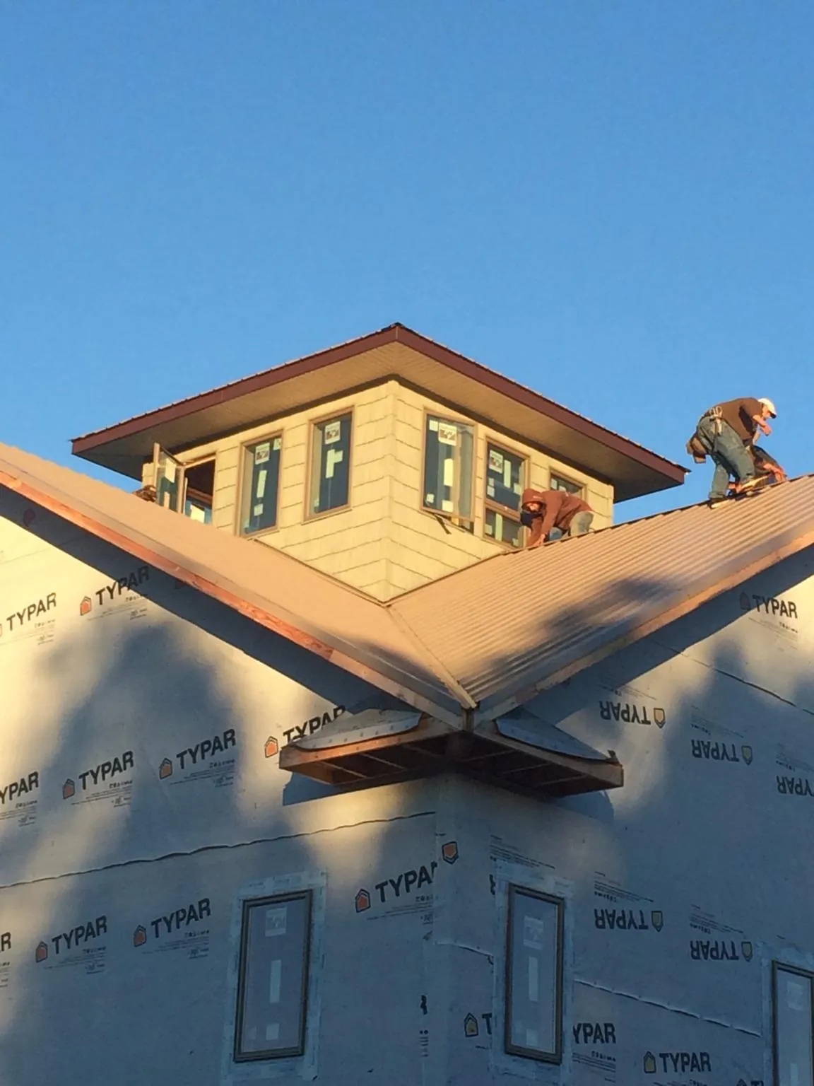 Roofers working around a rooftop cupola on a new metal roof at sunset — Roof Waterproofing in Morrisville by Roofing Brothers